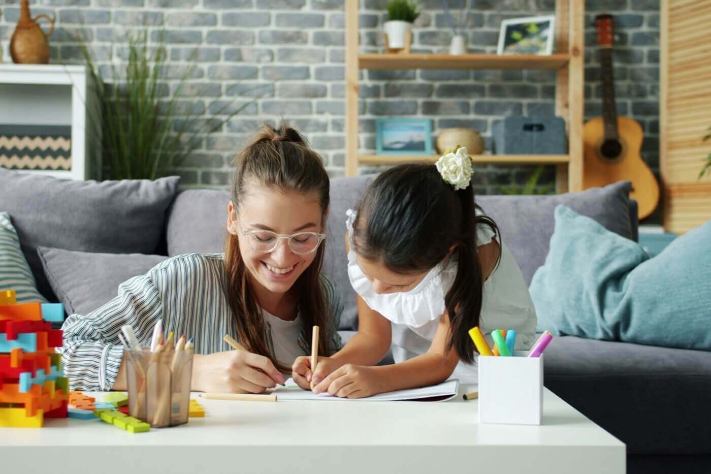 A woman and a young girl drawing together with coloured pencils at a table.